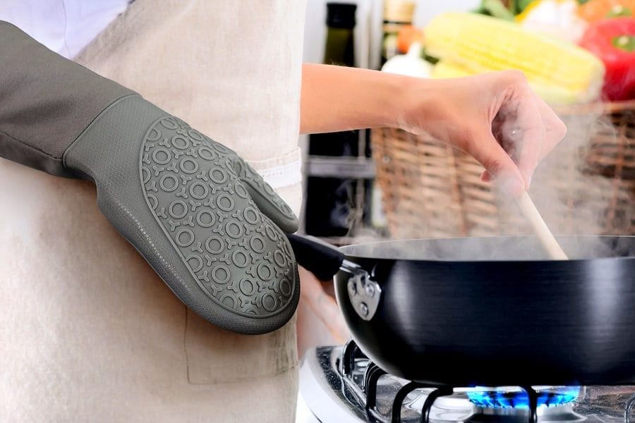 A long-cuffed silicone oven mitt lifting a pan over a gas flame