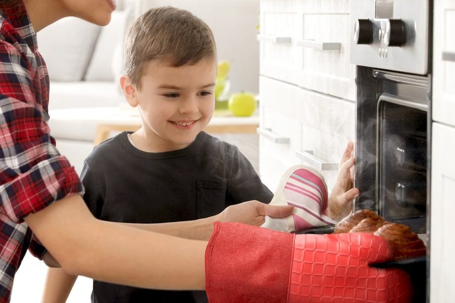 A red silicone mitt lifting a loaf of bread out of a hot oven